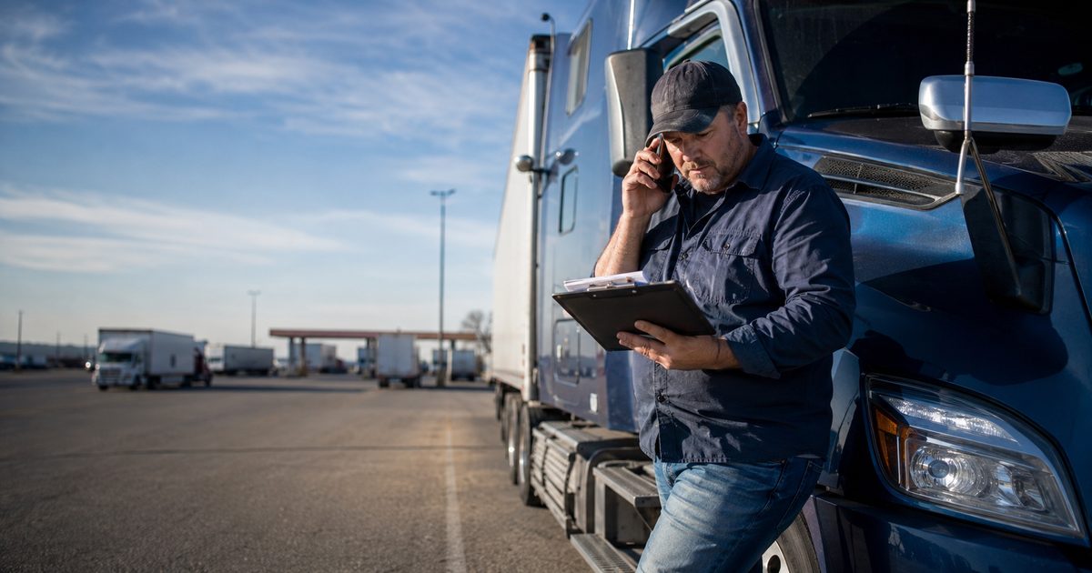 Owner-operator standing beside his semi-truck reviewing a dispatched load